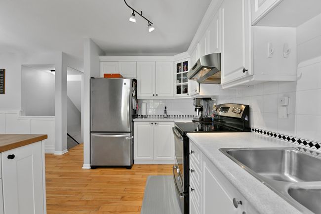 Kitchen with white cabinets, light wood-style flooring, exhaust hood, and appliances with stainless steel finishes | Image 13