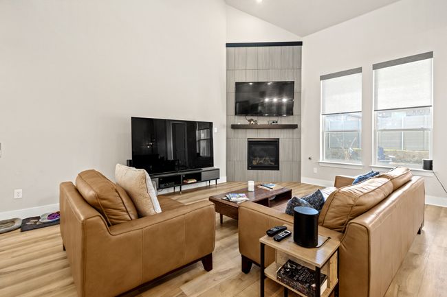 Living area with a large fireplace, light wood-type flooring, baseboards, and vaulted ceiling | Image 6