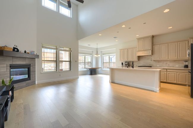 Kitchen featuring light wood-style flooring, open floor plan, a towering ceiling, light countertops, and a fireplace | Image 7