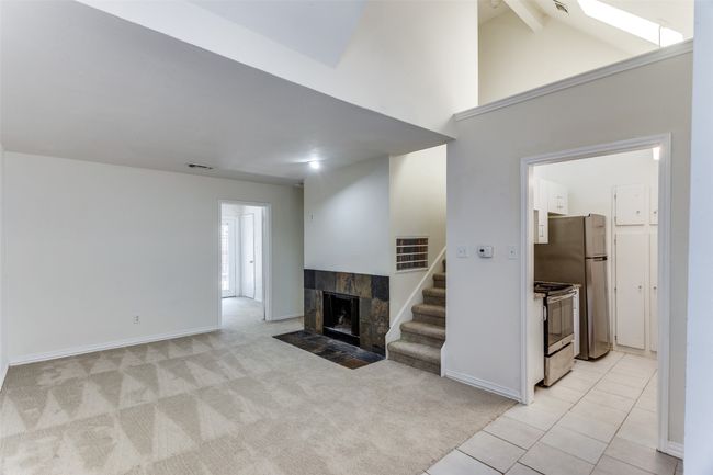 Unfurnished living room featuring a tiled fireplace, high vaulted ceiling, light colored carpet, stairway, and light tile patterned floors | Image 4