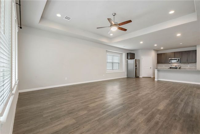 Unfurnished living room with a tray ceiling, a ceiling fan, dark wood-style flooring, and recessed lighting | Image 10