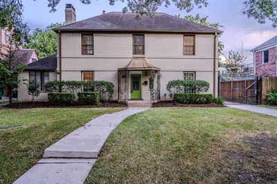 Two-story traditional brick home featuring a symmetrical facade with a central entryway, flanked by multi-pane windows and framed by manicured shrubbery. The property includes a well-kept lawn and a pathway leading to the vibrant front door. | Image 1