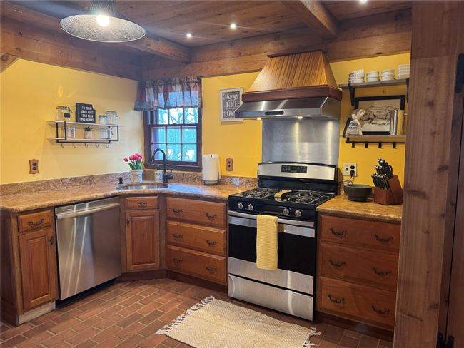 Kitchen with beamed ceiling, stainless steel appliances, wall chimney range hood, open shelves, and a sink | Image 10