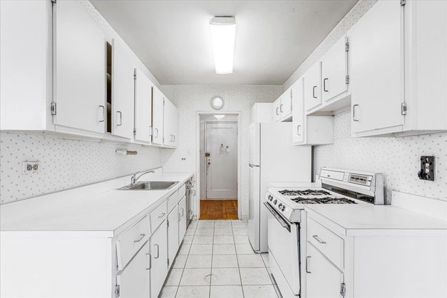 Kitchen featuring white gas range, light countertops, light tile patterned floors, white cabinets, and tasteful backsplash | Image 8