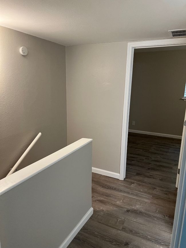 Corridor with dark wood-type flooring, visible vents, baseboards, and an upstairs landing | Image 15