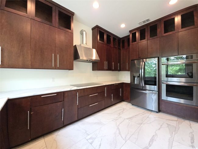 Kitchen with stainless steel appliances, wall chimney exhaust hood, light marble finish floors, recessed lighting, and dark brown cabinets | Image 5