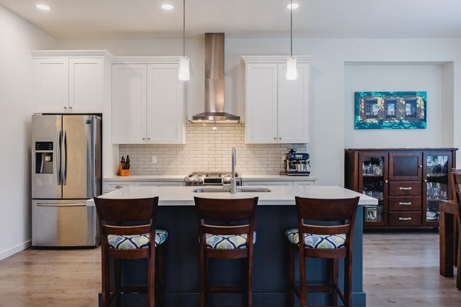 Kitchen featuring an island with sink, stainless steel fridge with ice dispenser, light countertops, wall chimney range hood, and light wood-style floors | Image 8