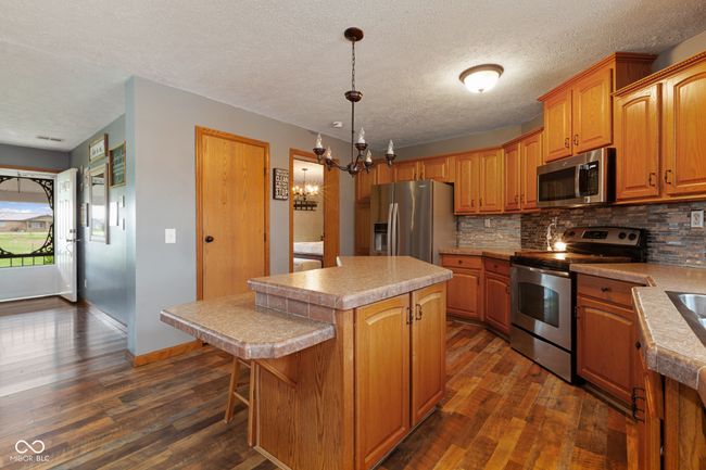 kitchen featuring dark wood finished floors, a center island, appliances with stainless steel finishes, a notable chandelier, and backsplash | Image 8