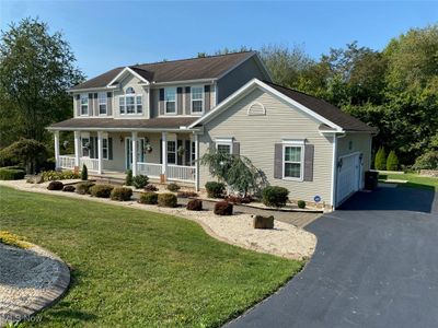 Colonial home featuring central AC unit, a garage, a front yard, and a porch | Image 1