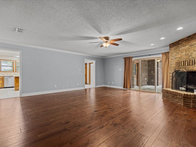 Unfurnished living room featuring a ceiling fan, a fireplace, wood-type flooring, a textured ceiling, and ornamental molding | Image 14