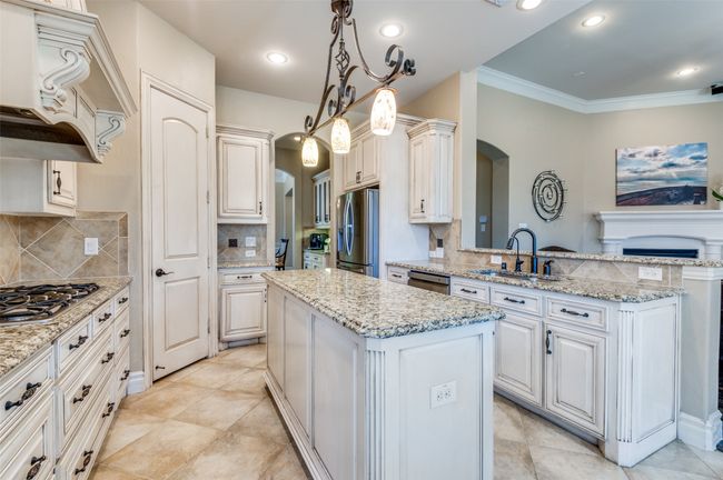 Kitchen with custom range hood, a sink, a center island, arched walkways, and appliances with stainless steel finishes | Image 16