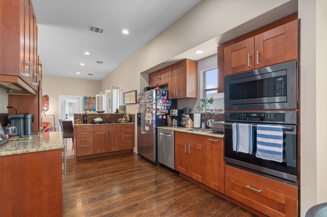 Kitchen featuring dark wood-style flooring, a sink, visible vents, light stone countertops, and appliances with stainless steel finishes | Image 6