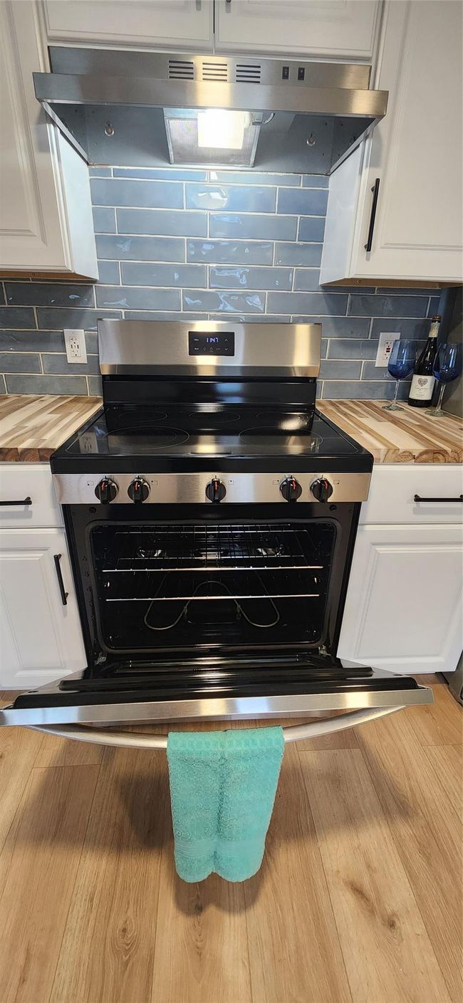 Kitchen featuring wood counters, extractor fan, white cabinetry, and electric range | Image 7