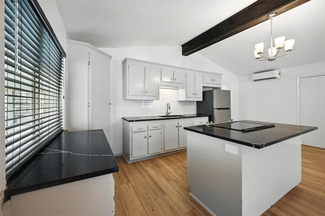 Kitchen with freestanding refrigerator, dark countertops, an AC wall unit, backsplash, and light wood finished floors | Image 9