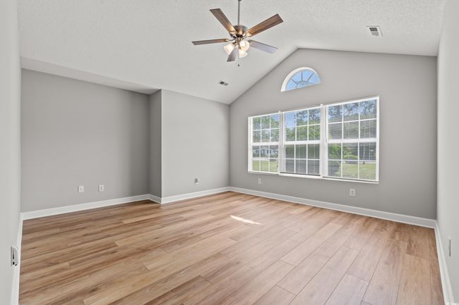 Empty room with ceiling fan, light wood finished floors, and vaulted ceiling | Image 9