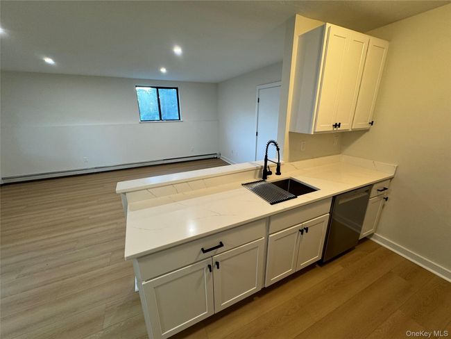 Kitchen with light wood-type flooring, a peninsula, dishwasher, white cabinetry, and a baseboard heating unit | Image 18