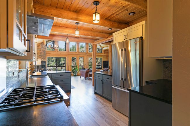Kitchen featuring freestanding refrigerator, dark countertops, stovetop, gray cabinetry, and wood ceiling with exposed beams | Image 5