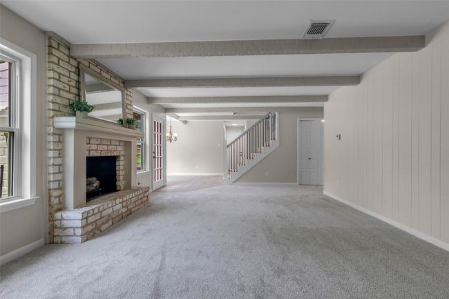 This inviting family room features a carpeted staircase with elegant railings, exposed ceiling beams, and a brick accent wall with a fireplace. Natural light pours in through large windows, and there's built-in cabinetry for storage. | Image 17