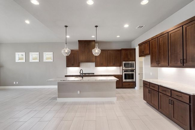 Kitchen featuring stainless steel appliances, decorative backsplash, a center island with sink, light stone counters, and hanging light fixtures | Image 9
