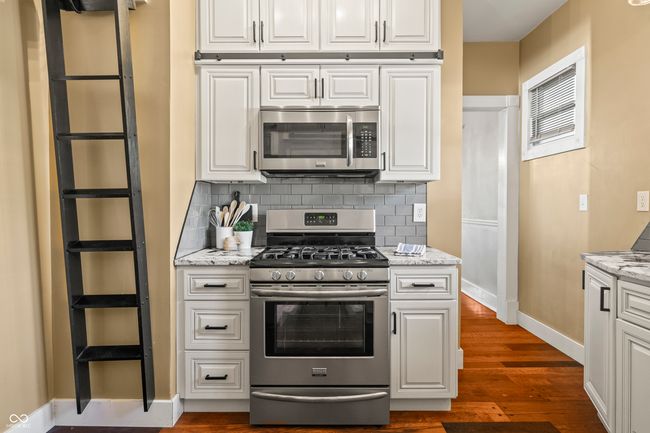 kitchen featuring white cabinetry, stainless steel appliances, backsplash, and light stone counters | Image 20