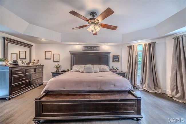 Bedroom with wood finished floors, a tray ceiling, and ceiling fan | Image 27