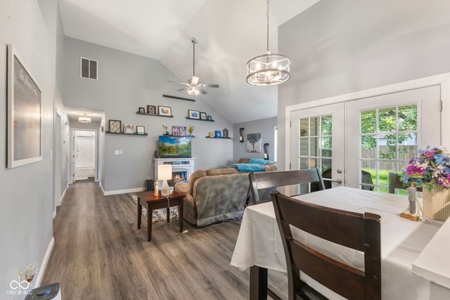 dining room featuring a chandelier, wood finished floors, ceiling fan, high vaulted ceiling, and a warm lit fireplace | Image 13