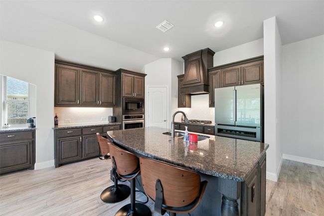 Kitchen with stainless steel appliances, dark brown cabinetry, light wood finished floors, backsplash, and vaulted ceiling | Image 12