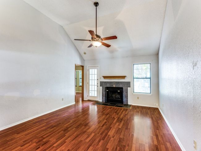 Unfurnished living room with plenty of natural light, a ceiling fan, wood finished floors, a fireplace, and high vaulted ceiling | Image 9