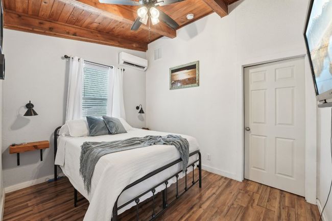 Bedroom featuring a wall mounted AC, wood ceiling with exposed beams, wood finished floors, baseboards, and a ceiling fan | Image 22