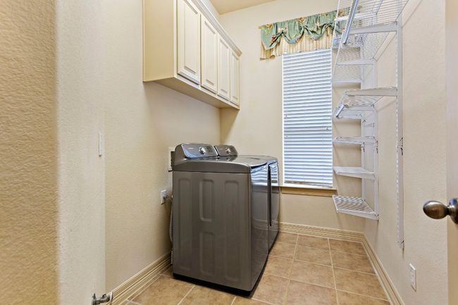 Clothes washing area featuring light tile patterned floors, baseboards, cabinet space, and independent washer and dryer | Image 26