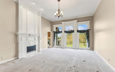 Great room with light carpet, chandelier, ornamental molding, and large fireplace | Image 3