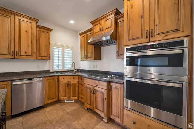 Kitchen with brown cabinets, a sink, appliances with stainless steel finishes, under cabinet range hood, and recessed lighting | Image 8