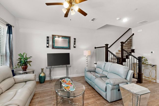 Living room with ceiling fan, wood tiled floors, and stairs | Image 5