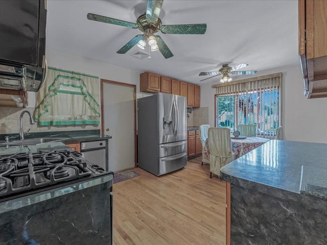 Kitchen with stainless steel refrigerator with ice dispenser, ceiling fan, brown cabinets, and dark countertops | Image 6