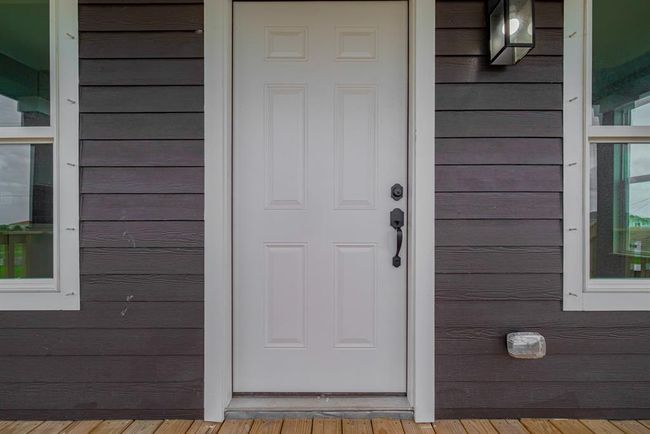 A closer look at the white front door reveals fine details illuminated by sconce lighting, standing out beautifully against the dark siding for a modern coastal contrast. | Image 5