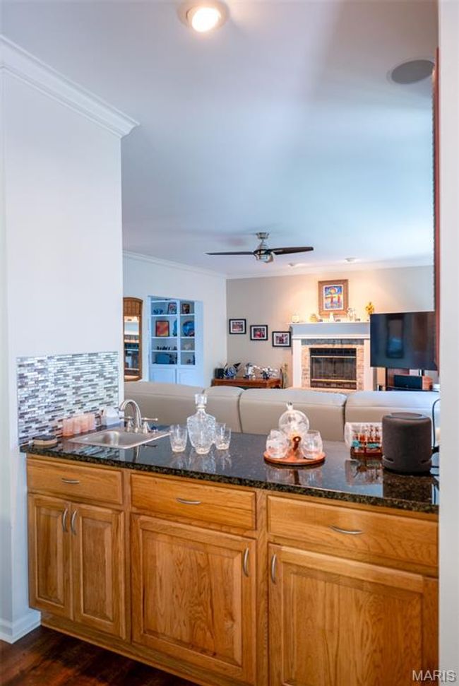 Kitchen with ornamental molding, dark stone countertops, open floor plan, dark wood-type flooring, and a ceiling fan | Image 12