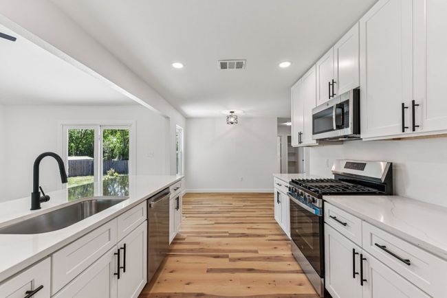 Kitchen featuring white cabinets, recessed lighting, appliances with stainless steel finishes, light wood-type flooring, and light stone countertops | Image 12