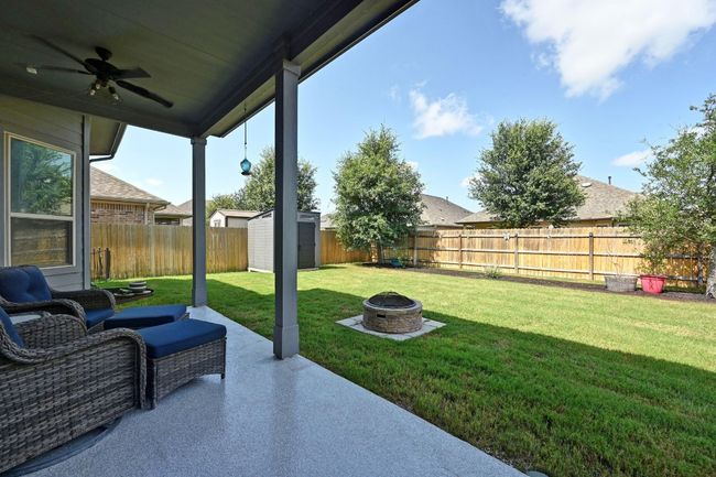 Large Fenced backyard with a fire pit, a ceiling fan, a storage unit, and a patio | Image 28