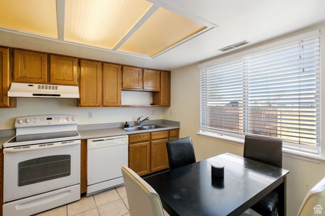 Kitchen with white appliances, under cabinet range hood, visible vents, brown cabinets, and a sink | Image 8