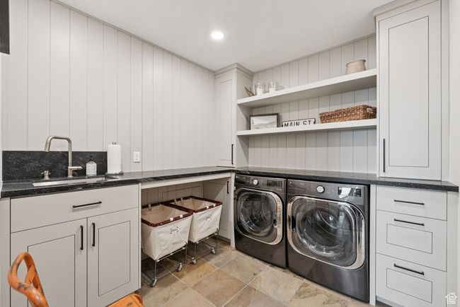 Laundry room featuring independent washer and dryer, cabinet space, wooden walls, and light stone finish floors | Image 78