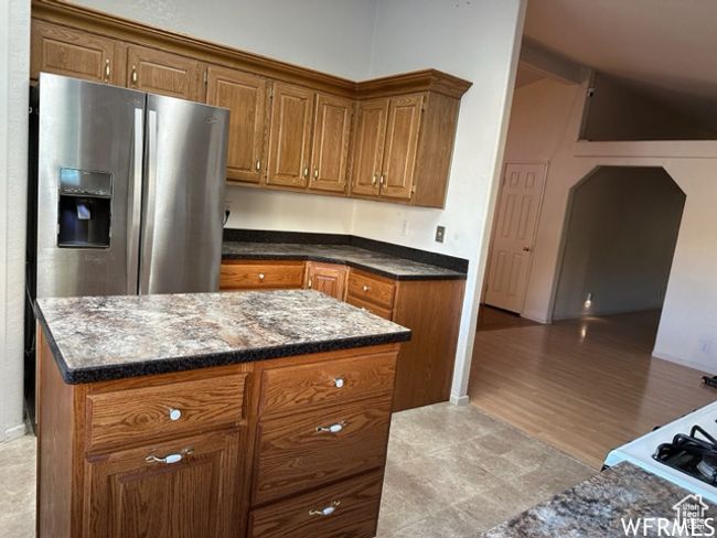 Kitchen featuring stainless steel fridge, a center island, brown cabinets, arched walkways, and dark stone counters | Image 49