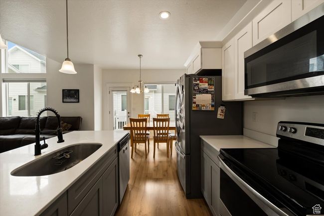 Kitchen with a sink, pendant lighting, stainless steel appliances, light countertops, and a notable chandelier | Image 7