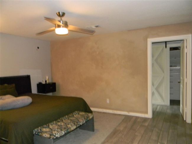 Primary bedroom featuring a ceiling fan, a mix of carpet and wood-style flooring and an ensuite bathroom with stand up shower, tub and double sink vanity with walk-in closet with a sliding barn door. | Image 14