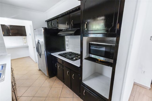 Kitchen featuring light tile patterned floors, black gas cooktop, tasteful backsplash, ornamental molding, and stainless steel fridge with ice dispenser | Image 4
