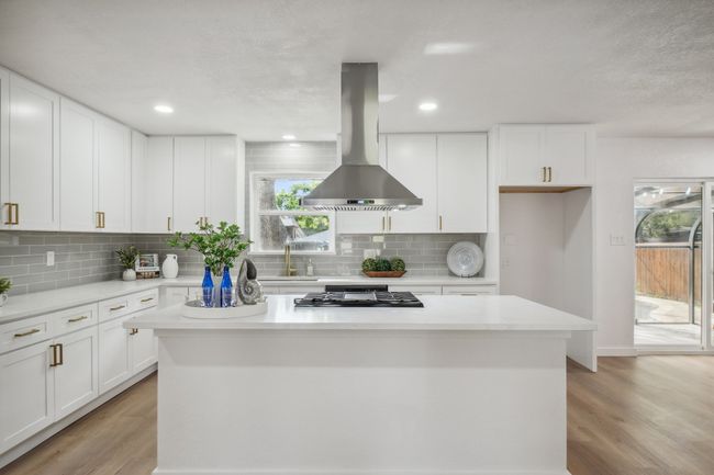 Kitchen featuring island range hood, gas cooktop, a center island, backsplash, and white cabinets | Image 14