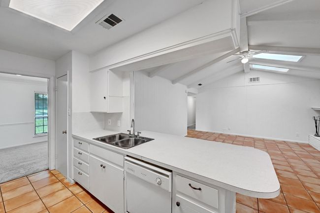 Kitchen with light tile patterned floors, visible vents, white dishwasher, a sink, and a peninsula | Image 14