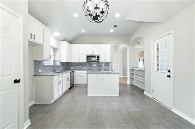 Kitchen with arched walkways, tasteful backsplash, a center island, white cabinets, and vaulted ceiling | Image 24