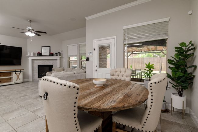 Dining area and living room with a ceiling fan, baseboards, a gas log fireplace, vaulted ceiling, large windows with coverings and ornamental molding | Image 5