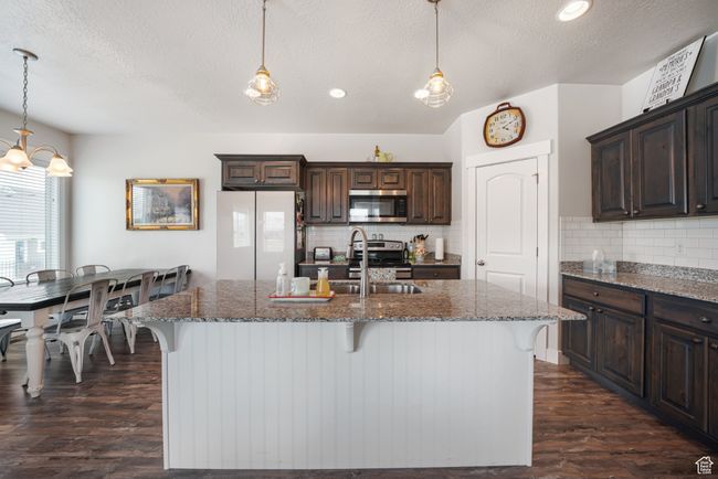Kitchen featuring stainless steel appliances, a textured ceiling, dark brown cabinets, a kitchen bar, and dark wood-type flooring | Image 7