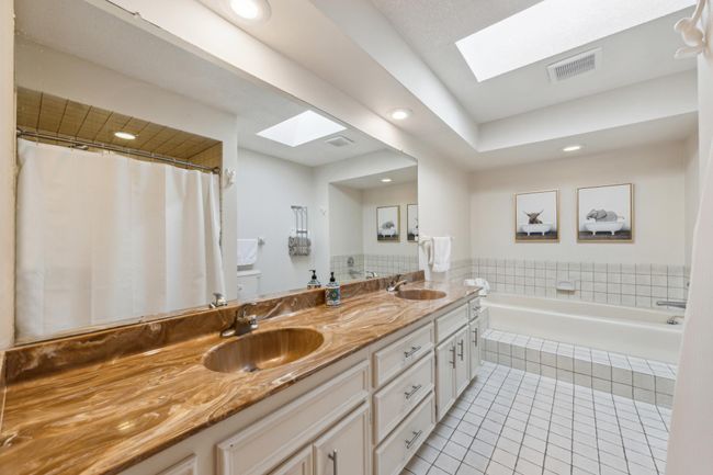 Spacious primary bathroom featuring a dual-sink vanity with marble-style like countertops, soaking tub, separate shower, and natural light from overhead skylights. | Image 15